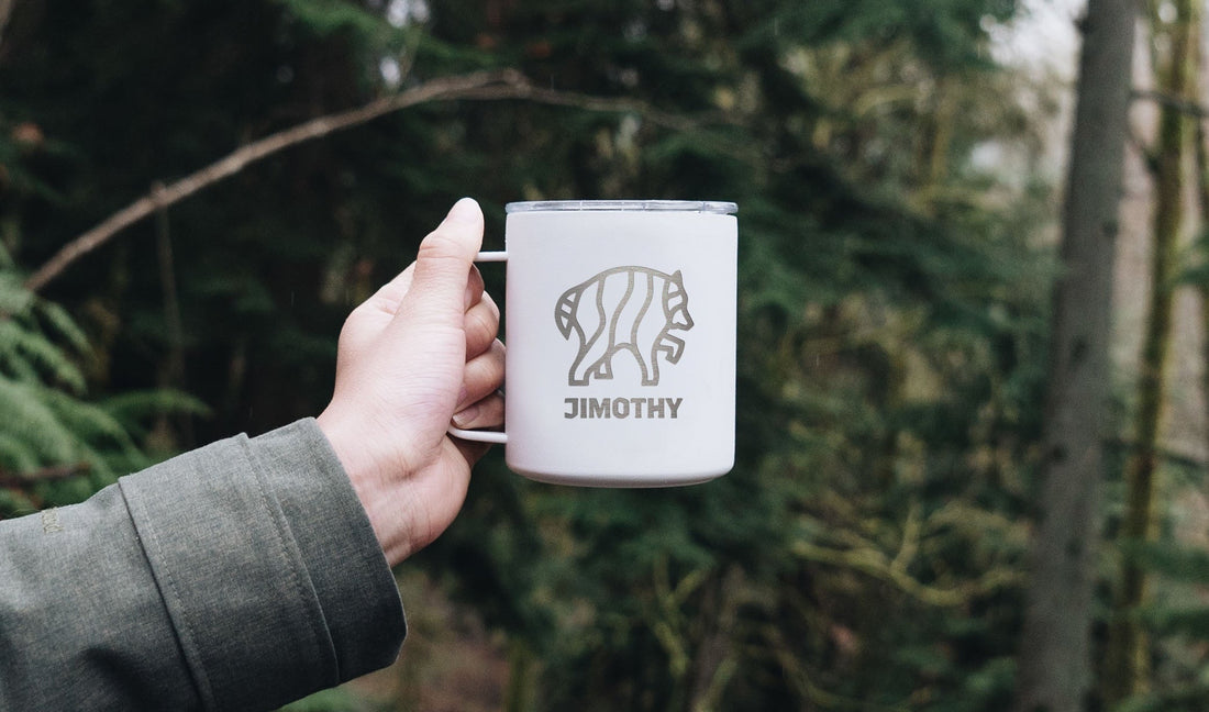 hand holding up white camp cup with Jimothy engraved in forest