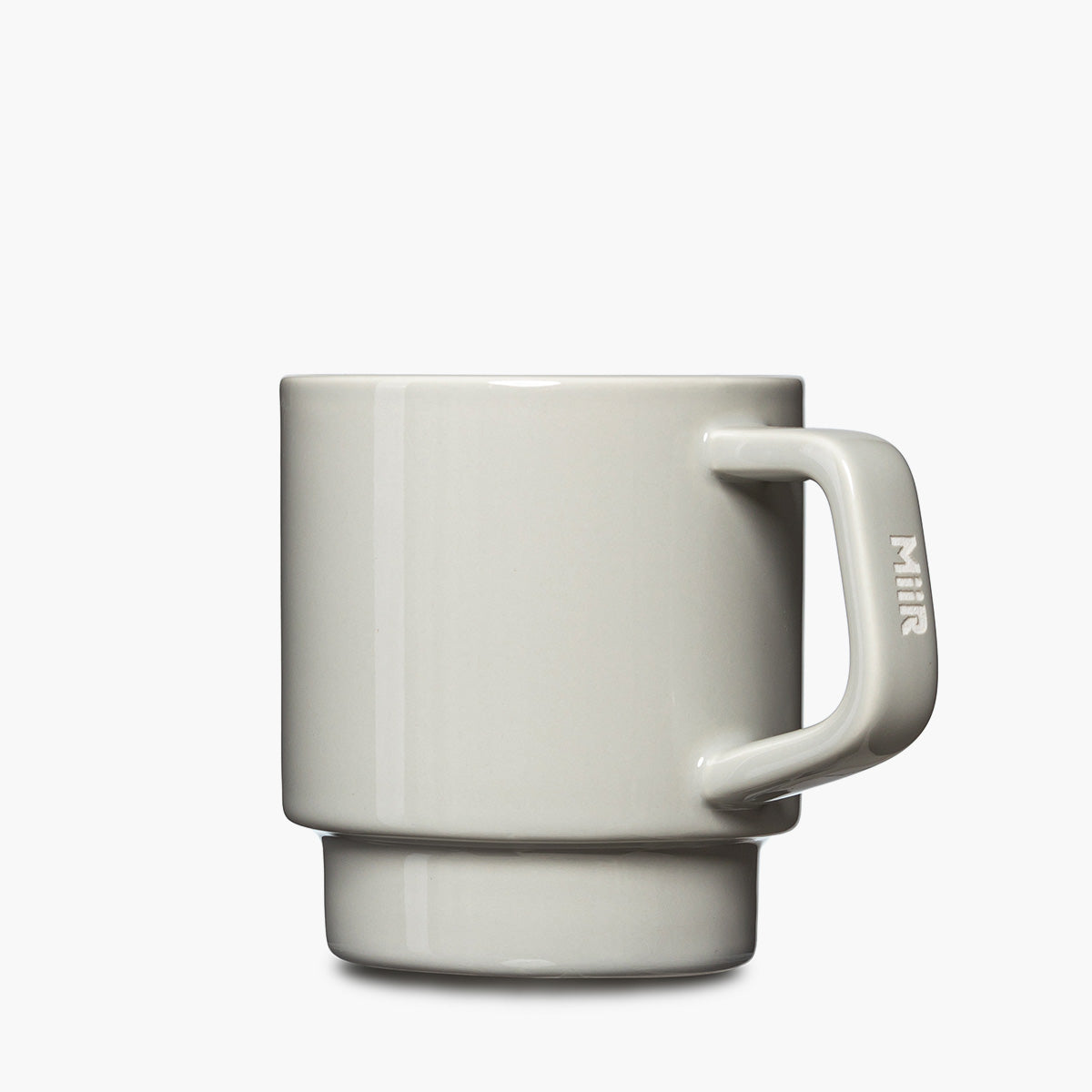 A minimalist ceramic mug in a light gray color, featuring a stacked two-tiered design and a thick handle with the brand name 'MiiR' etched vertically on it.