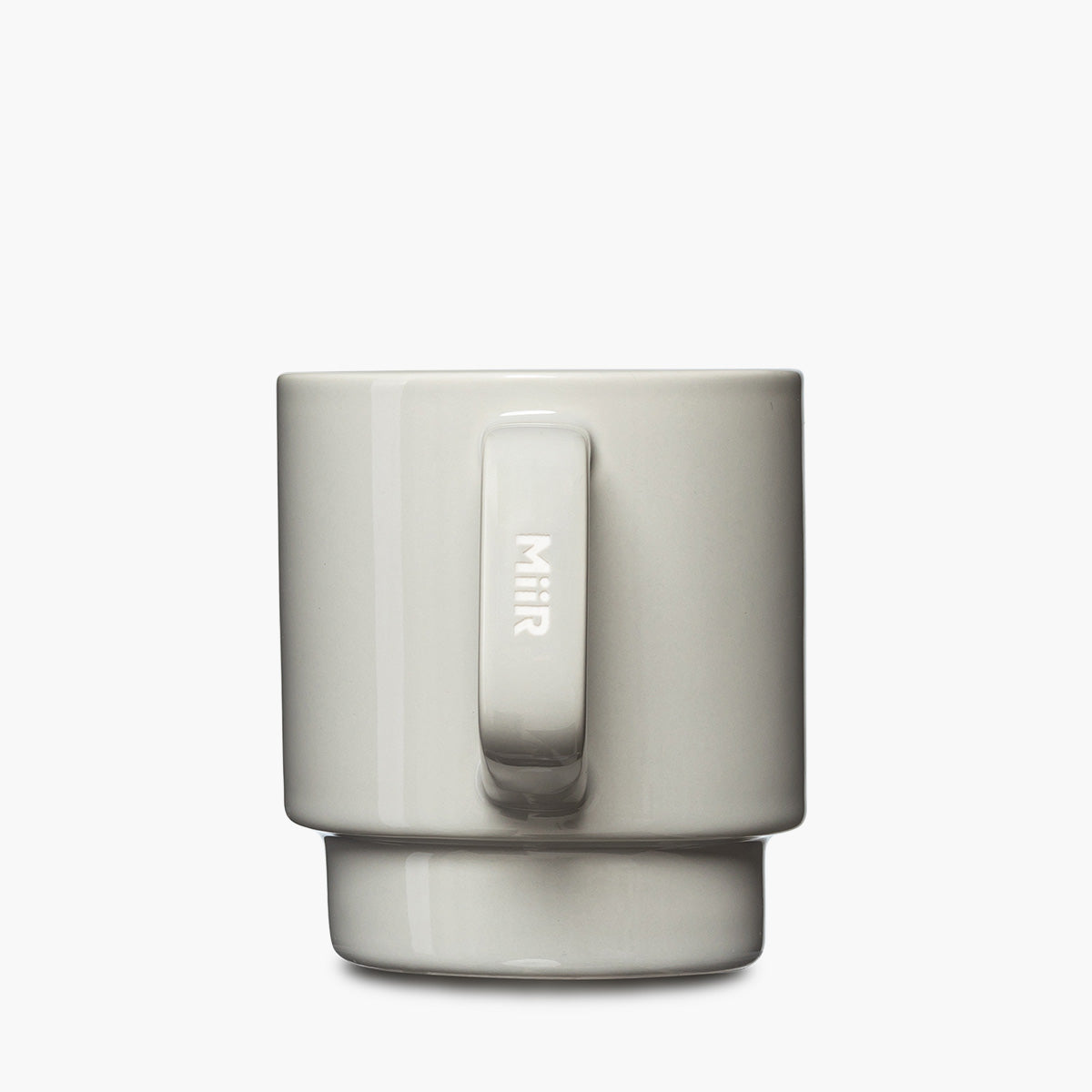 A minimalist ceramic mug in a light gray color, featuring a matching handle and a matching base ring, with the brand name 'MiiR' etched vertically on the handle.