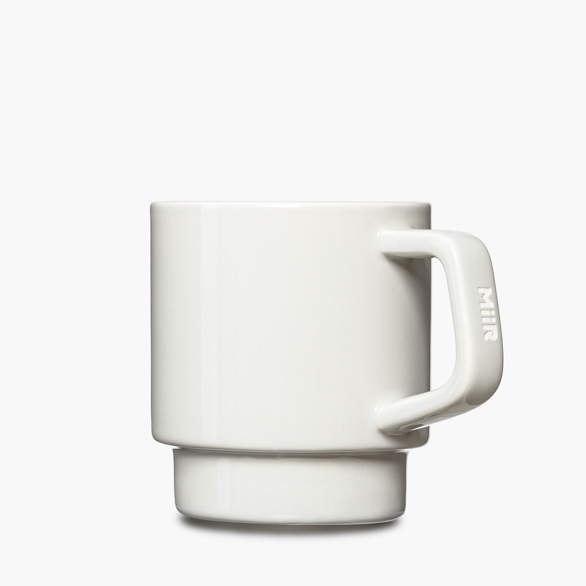 A minimalist white ceramic mug with a thick handle and a matching base, featuring the brand name 'MiiR' etched vertically on the handle.