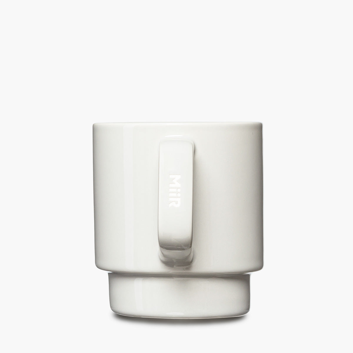 A minimalist white ceramic mug with a matching base, featuring a vertical handle and the word 'MIR' etched vertically on the handle