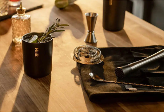 A cocktail barware tool set and cup on a wooden table
