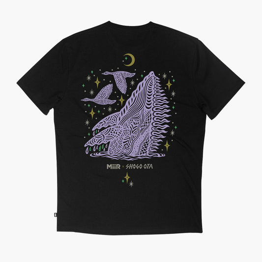 A black short-sleeve t-shirt with a large graphic print on the front. The graphic features a stylized purple whale with intricate line patterns, two birds, a crescent moon, and stars in purple, green, and gold, with the text 'MiiR - SHOGO OTA' printed below.