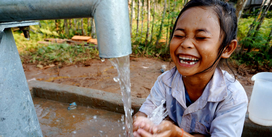 A child in rural Laos smiling while fresh water pours from a spigot into their hands.